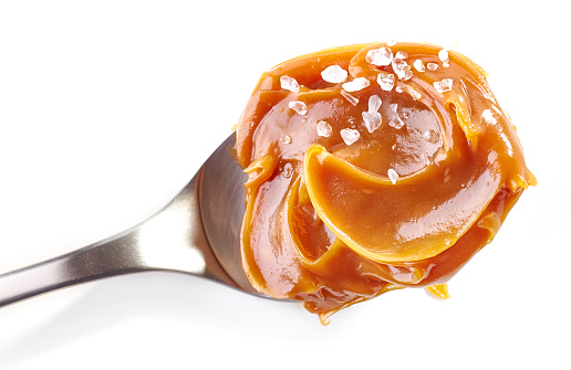 spoon of soft homemade salted caramel isolated on white background, top view