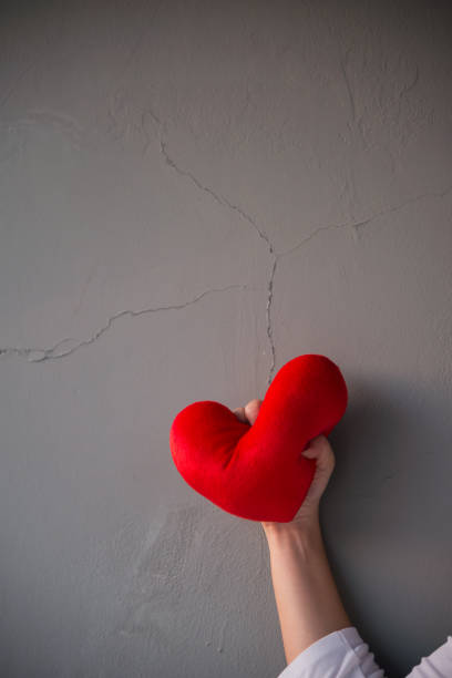 istock Red heart pillow was squeezed angrily over cracked grey wall background showing fail love on Valentines day 669247164