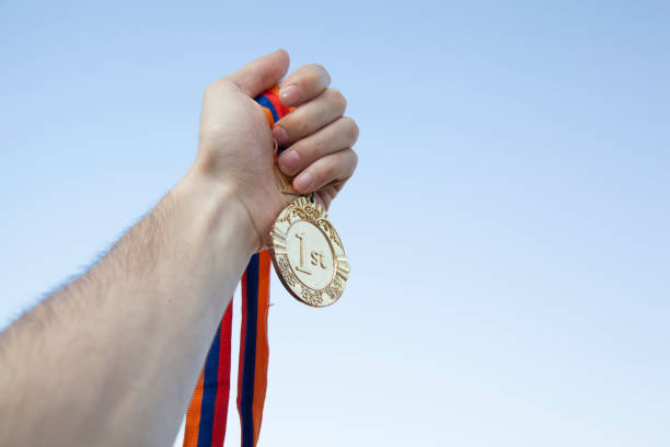 istock man hand raised, holding gold medal against sky 669256948