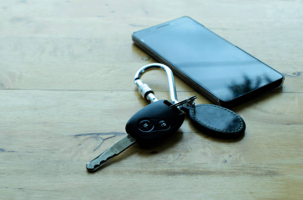 a car key with a wireless remote to lock and unlock the alarm system of the car and a black cellphone isolated on a white background with a copy space, selective focus of car keys and mobile phone
