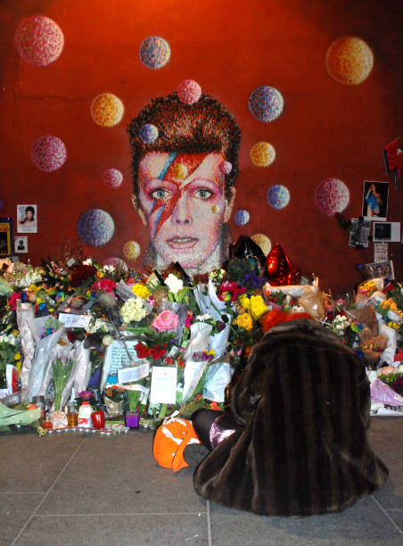 Fan mourns the death of David Bowie by his mural in Brixton, London Ziggy Stardust fan sits by flowers and pays respect to one of London's most famous icons brixton photos stock pictures, royalty-free photos & images