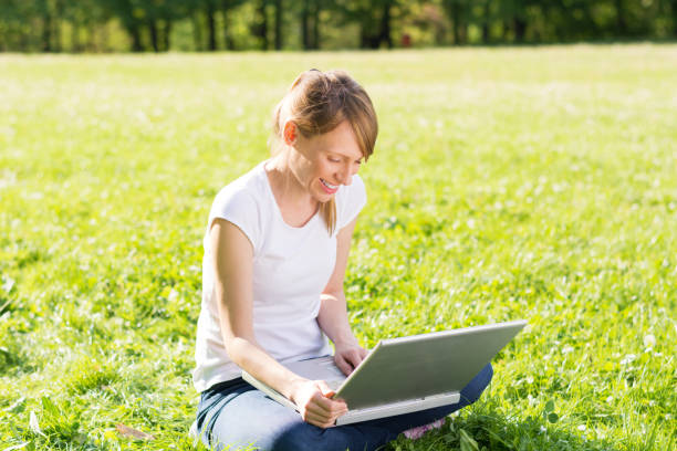 istock Beautiful smiling young woman sitting on a meadow and using her laptop 669280918