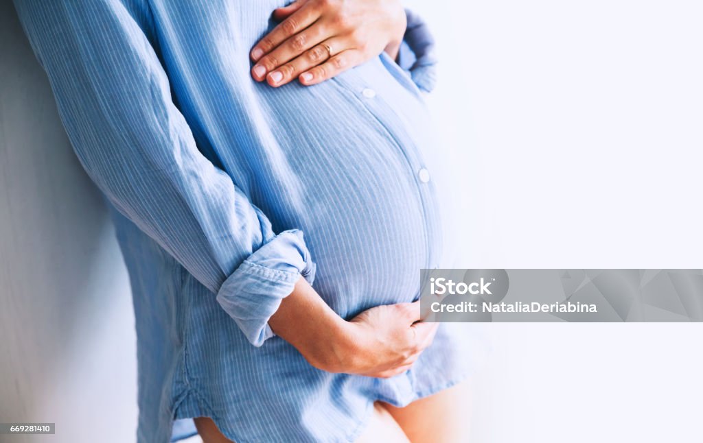 Pregnant woman holds hands on belly at home interiors. Pregnant woman holds hands on belly at home interiors. Pregnancy, parenthood, preparation and expectation concept. Close-up, copy space, indoors. Pregnant Stock Photo