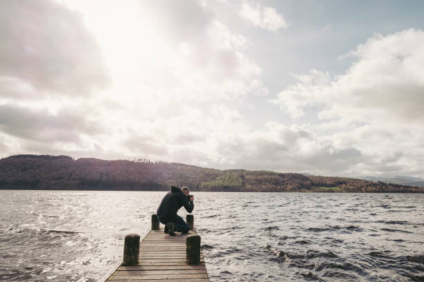 istock Man on a jetty overlooking Lake Windermere taking a photograph. 669305394