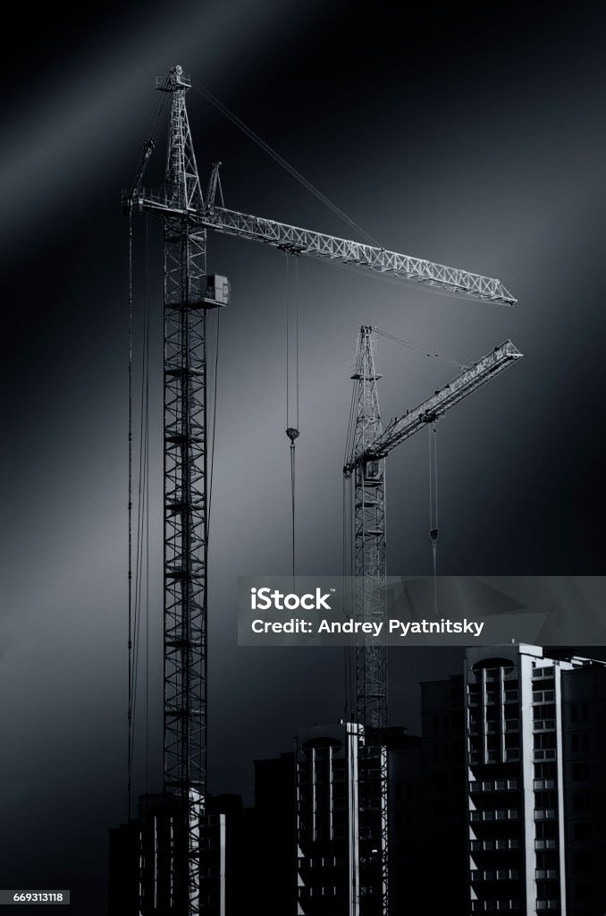 Construction cranes standing on the black background Construction cranes stand in the background of the buildings Black And White Stock Photo