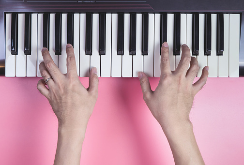 Hand playing Music keyboard on pink background, above view.