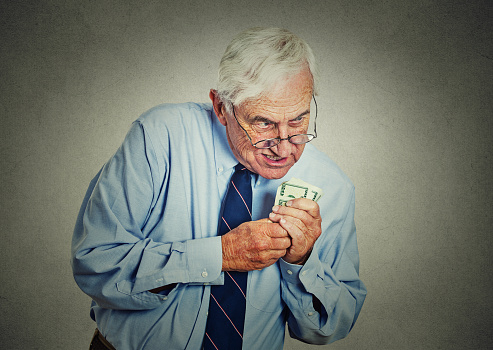 Closeup portrait greedy senior executive, CEO, boss, old corporate employee, mature man, holding dollar banknotes isolated on gray wall background. Negative human emotion facial expression