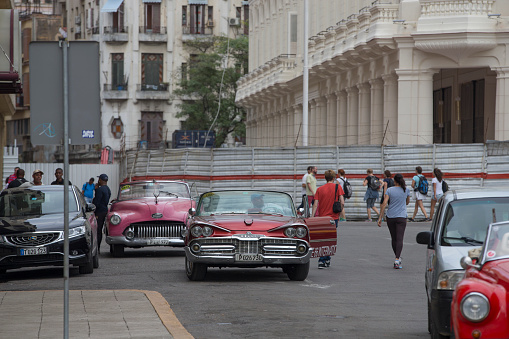 Vintage cars are driving on the street. Incidental people on the background.