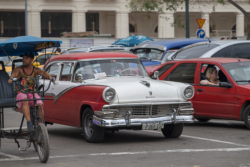 Vintage cars are driving on the street. Incidental people on the background.