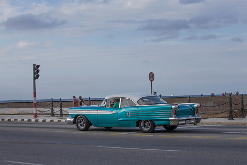 Vintage cars are driving on the street. Incidental people on the background.