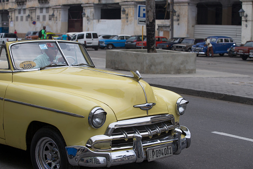 Havana, Cuba - January 28, 2017: Diferent color vintage cars either driving on the street or parking on the street. Incidental people on the background.