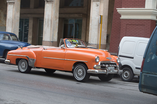 Havana, Cuba - January 28, 2017: A pretty orange color vintage car on the street. Incidental people on the background.