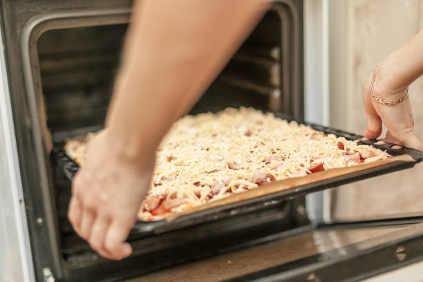 istock Woman puts tray with raw pizza into oven 669380876