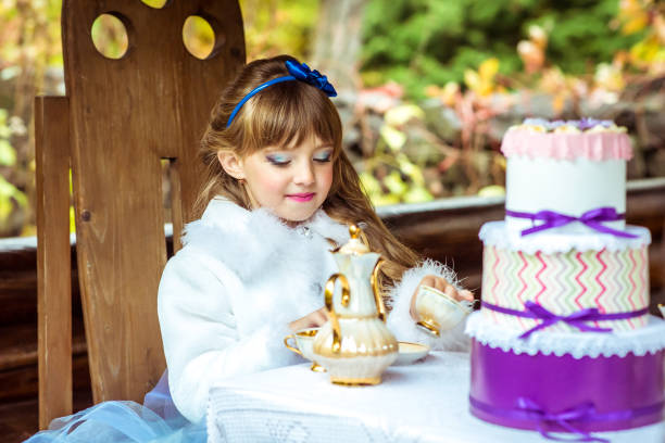 vista frontal de uma menina bonita no cenário da alice no país das maravilhas, segurando uma xícara de chá na mesa - little girls alice in wonderland child fairy tale - fotografias e filmes do acervo