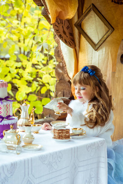 vista frontal de uma menina bonita no cenário da alice no país das maravilhas, segurando uma xícara de chá na mesa - little girls alice in wonderland child fairy tale - fotografias e filmes do acervo