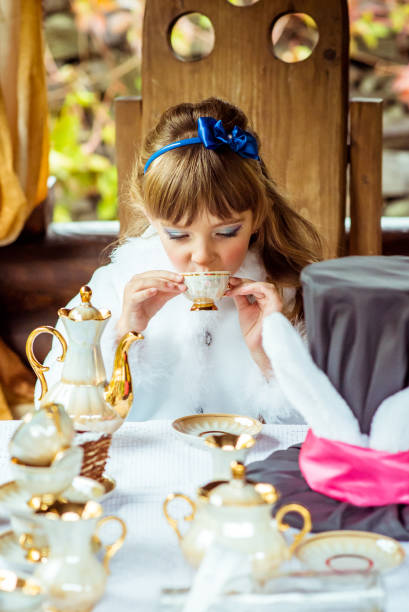 vista frontal de uma menina bonita no cenário da alice no país das maravilhas, beber um chá na mesa no parque - little girls alice in wonderland child fairy tale - fotografias e filmes do acervo
