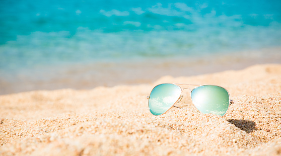 Beautiful background of Turquoise Sea with men's sunglasses lying on the sand beach. The concept of Rest Vacation. Wide Horizontal Colorful Wallpaper with selective focus and copy space.