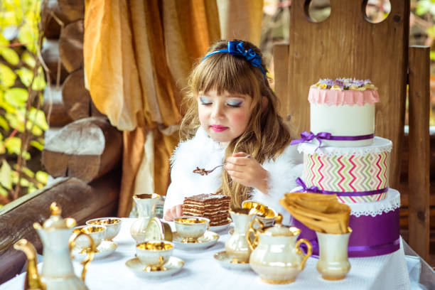 vista frontal de uma garotinha linda segurando um pedaço de bolo uma colher à mesa - little girls alice in wonderland child fairy tale - fotografias e filmes do acervo