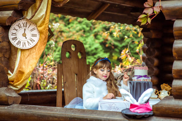 vista frontal de uma garotinha linda segurando um pedaço de bolo uma colher à mesa - little girls alice in wonderland child fairy tale - fotografias e filmes do acervo