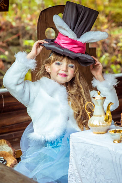 una bambina bella che tiene il cappello a cilindro con le orecchie come un coniglio sopra la testa a tavola - little girls alice in wonderland child fairy tale foto e immagini stock