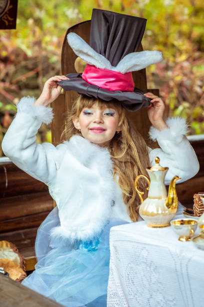 uma menina linda segurando chapéu de cilindro com orelhas como um coelho cabeça sobre a mesa - little girls alice in wonderland child fairy tale - fotografias e filmes do acervo