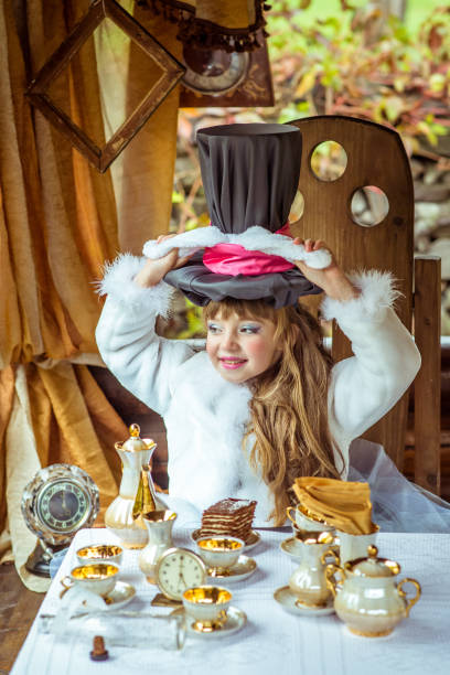 una bambina bella che tiene il cappello a cilindro con le orecchie come un coniglio sopra la testa a tavola - little girls alice in wonderland child fairy tale foto e immagini stock