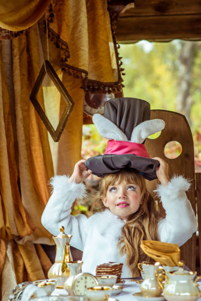 una bambina bella che tiene il cappello a cilindro con le orecchie come un coniglio sopra la testa a tavola - little girls alice in wonderland child fairy tale foto e immagini stock