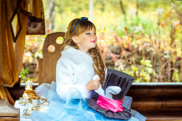 una bambina bella che tiene il cappello a cilindro con le orecchie come un coniglio tra le mani a tavola - little girls alice in wonderland child fairy tale foto e immagini stock