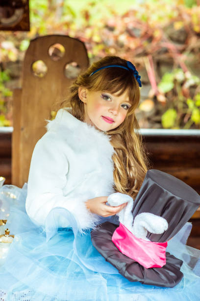 uma menina linda segurando o chapéu do cilindro com orelhas como um coelho nas mãos na mesa - little girls alice in wonderland child fairy tale - fotografias e filmes do acervo