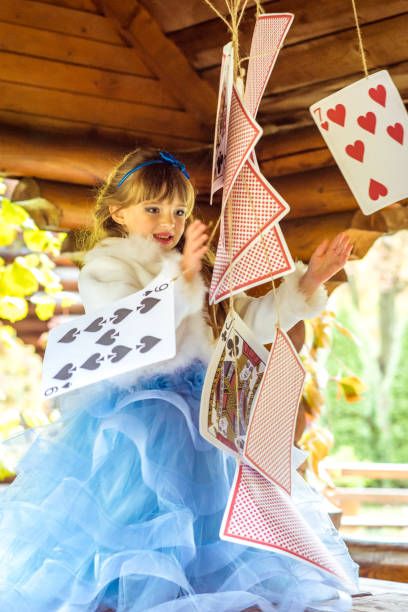 uma linda garotinha brincando e dançando com grandes jogando cartas na mesa - little girls alice in wonderland child fairy tale - fotografias e filmes do acervo