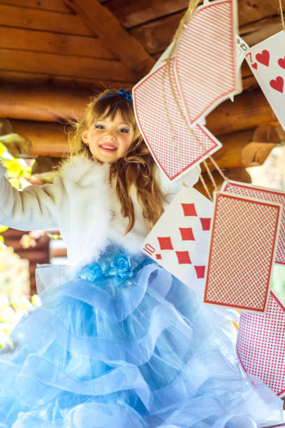 una bambina bella che gioca e balla con grandi carte da gioco sul tavolo - little girls alice in wonderland child fairy tale foto e immagini stock