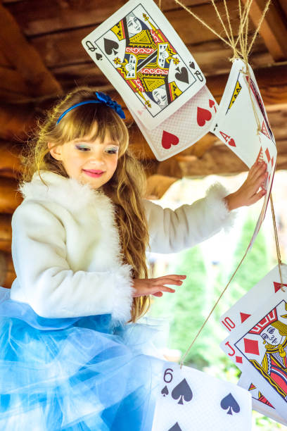 uma linda garotinha brincando e dançando com grandes jogando cartas na mesa - little girls alice in wonderland child fairy tale - fotografias e filmes do acervo