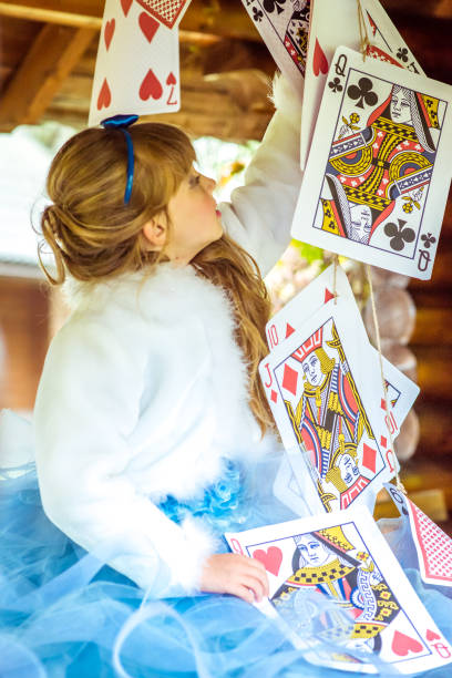 uma linda garotinha brincando e dançando com grandes jogando cartas na mesa - little girls alice in wonderland child fairy tale - fotografias e filmes do acervo