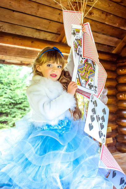 uma linda garotinha brincando e dançando com grandes jogando cartas na mesa - little girls alice in wonderland child fairy tale - fotografias e filmes do acervo