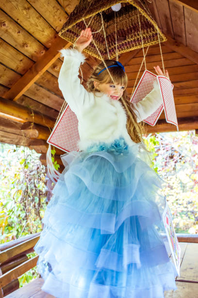 una bambina bella che gioca e balla con grandi carte da gioco sul tavolo - little girls alice in wonderland child fairy tale foto e immagini stock