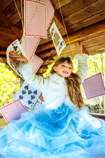 uma linda garotinha brincando e dançando com grandes jogando cartas na mesa - little girls alice in wonderland child fairy tale - fotografias e filmes do acervo