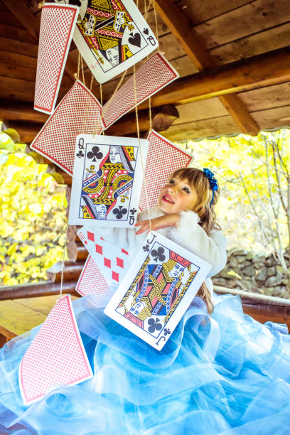 una bambina bella che gioca e balla con grandi carte da gioco sul tavolo - little girls alice in wonderland child fairy tale foto e immagini stock