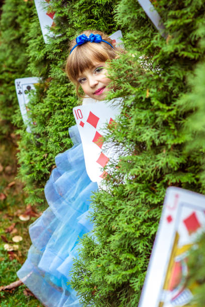 una bambina bellissima con un lungo vestito blu che guarda da sotto gli abeti - little girls alice in wonderland child fairy tale foto e immagini stock