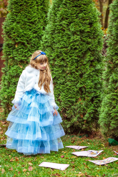 uma menina bonita em pé perto das árvores de abeto e olhar para as cartas de jogar - little girls alice in wonderland child fairy tale - fotografias e filmes do acervo