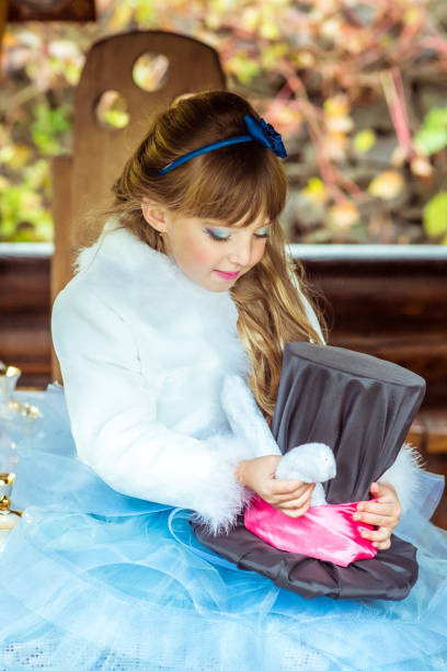 uma menina linda segurando o chapéu do cilindro com orelhas como um coelho nas mãos na mesa - little girls alice in wonderland child fairy tale - fotografias e filmes do acervo