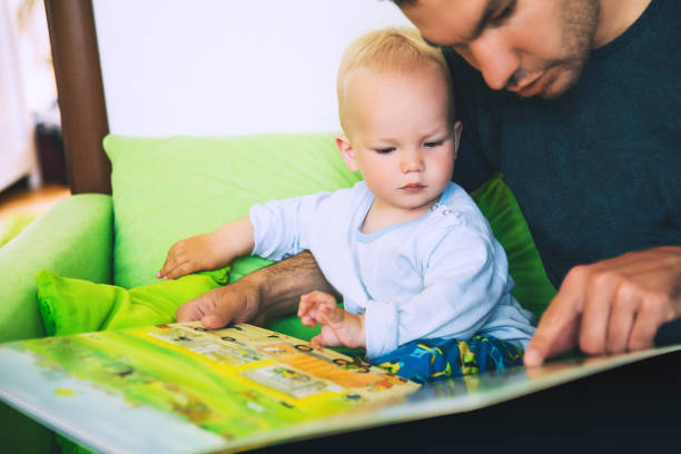 mały chłopiec czyta książkę z ojcem we wnętrzach domu. - baby book toddler reading zdjęcia i obrazy z banku zdjęć