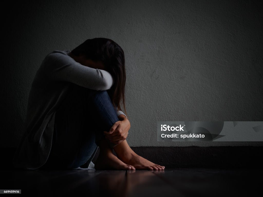 sad woman hug her knee and cry. Sad woman sitting alone in a empty room. Dark Stock Photo