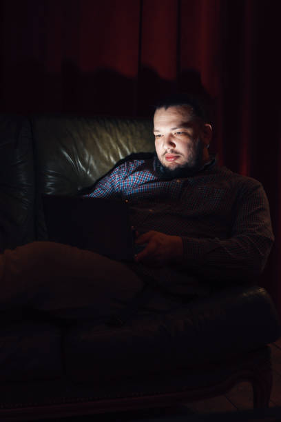 istock Young man with laptop rest on couch in dark room 669459910
