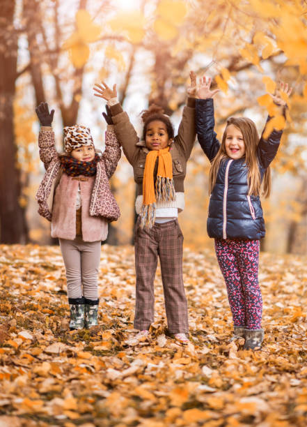 Full length of happy little girls in nature standing with raised arms and looking at camera.