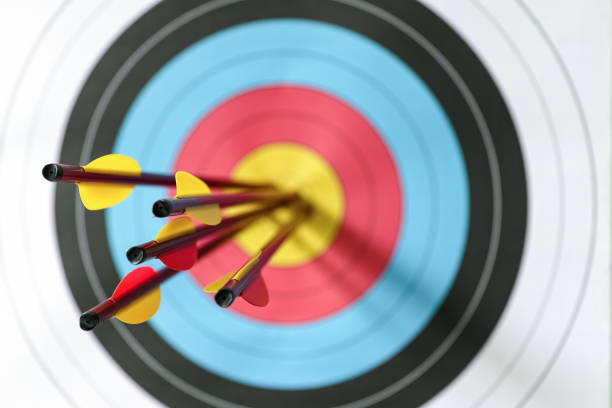 Five arrows in the bull's-eye of a sports target. Five arrows in the bull's-eye of an archery target. Selective focus with the focus being on the back end of the arrow, with an out of focus target in the background. Concept image being on target, strategy, aim, accomplishment, aiming for the bull's eye etc. archery photos stock pictures, royalty-free photos & images