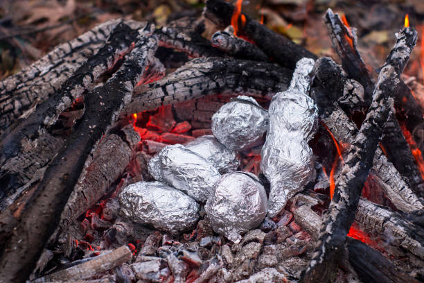 istock Baked potatoes wrapped with aluminum foil roasting in a bonfire. 669488324