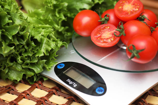 Fresh tomatoes on kitchen scales weighing Fresh tomatoes on kitchen scales weighing and measuring kitchen scale stock pictures, royalty-free photos & images