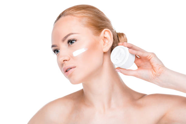 portrait of woman showing face cream and looking away on white