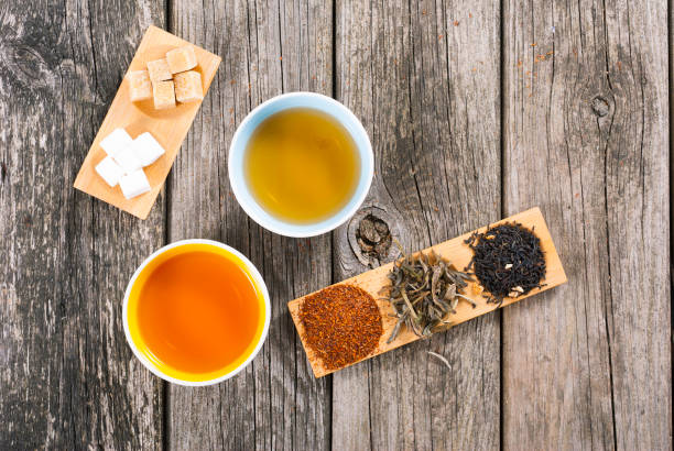 Tea on weathered wooden table two cups of japanese tea, sugar nubs and crops on bamboo serving tray on old rusty wooden table nub stock pictures, royalty-free photos & images
