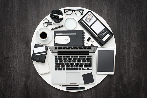 Business and office desktop equipment in a white circle on a dark elegant desk, flat lay